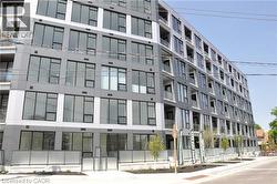 Contemporary multi-story building featuring a facade of grey and white panels, extensive black-framed windows, and glass balcony railings - 