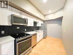 Kitchen featuring stainless steel appliances, white cabinetry, a black hexagonal tile backsplash, light countertops, and wood-finish flooring - 