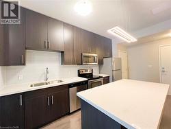 Modern kitchen featuring dark wood-finish cabinetry, stainless steel appliances, a white subway tile backsplash, light-toned countertops, and an expansive kitchen island - 