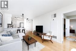 Open-concept living area featuring light wood-finish flooring, white walls, a modern multi-directional ceiling light fixture, and a kitchen bar with pendant lighting - 