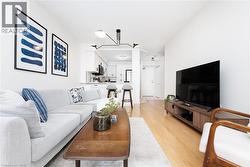 Open-concept living space featuring wood-finish flooring, white walls, and a modern kitchen with white cabinetry and black hardware - 