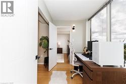 Dedicated workspace featuring expansive window panels, wood-finish flooring, a built-in wood desk, and modern wall sconce lighting - 