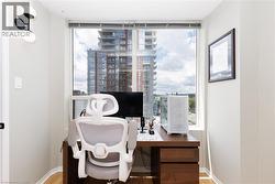 Dedicated workspace featuring a large window, wood-finish flooring, a contemporary wall sconce, and a built-in wood desk with drawers - 