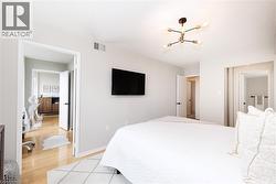 Bedroom featuring a contemporary ceiling light fixture, wall-mounted television, and light gray wall paint - 
