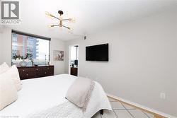 Bedroom featuring a modern sputnik chandelier, a wall-mounted television, a large window, light-toned walls, and wood-finish flooring - 