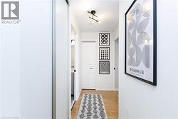 Hallway featuring light wood-finish flooring, white walls, sliding closet doors, a modern ceiling light fixture, and interior doors with black hardware - 