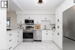 U-shaped kitchen featuring white shaker cabinetry with matte black hardware, stainless steel appliances, a white subway tile backsplash, and light-toned countertops - 