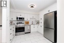 Modern kitchen featuring white cabinetry, stainless steel appliances, light-toned countertops, a subway tile backsplash, and large format floor tiles - 