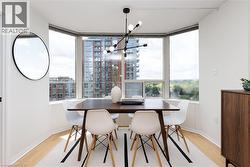 Dining area featuring expansive bay windows, wood-finish flooring, a modern linear chandelier, a built-in wood-tone cabinet, and white walls - 
