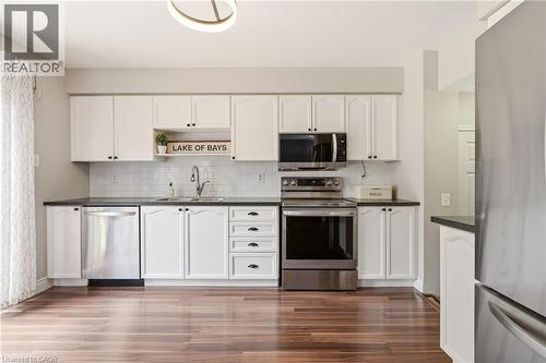Kitchen featuring white shaker-style cabinetry, stainless steel appliances, dark countertops, a subway tile backsplash, and wood-finish flooring - 2089 Broadleaf Crescent, Burlington, ON 
