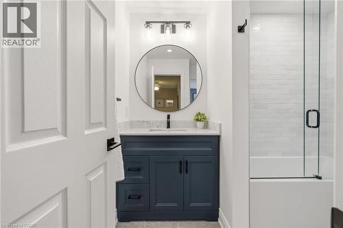 Bathroom featuring a dark blue vanity cabinet with a light-toned countertop, a circular mirror, and a contemporary light fixture - 2089 Broadleaf Crescent, Burlington, ON 