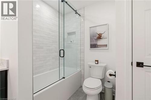 Bathroom featuring a white subway-tiled shower with a clear glass sliding door, a built-in shower niche, and a white porcelain toilet - 2089 Broadleaf Crescent, Burlington, ON 