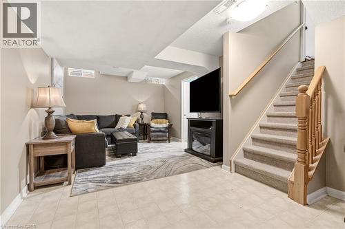 Lower level living area featuring light-toned walls, tiled flooring, and a carpeted staircase with a wooden banister - 2089 Broadleaf Crescent, Burlington, ON 