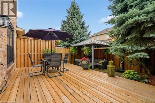 Expansive wooden deck featuring a privacy fence, mature evergreen trees, and a dedicated covered seating area - 2089 Broadleaf Crescent, Burlington, ON 