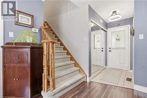 Entryway featuring a carpeted staircase with wood banister, wood-finish flooring, and a tiled landing - 2089 Broadleaf Crescent, Burlington, ON 