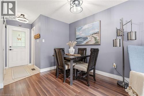 Dining area featuring wood-finish flooring, a contemporary ceiling light fixture, and a white paneled entry door with frosted glass detailing - 2089 Broadleaf Crescent, Burlington, ON 