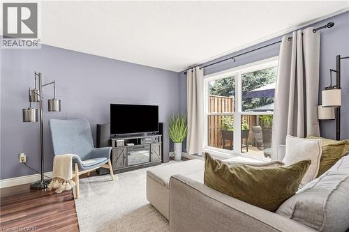 Spacious living area featuring wood-finish flooring, a large window overlooking a private fenced yard, and light-toned walls - 2089 Broadleaf Crescent, Burlington, ON 