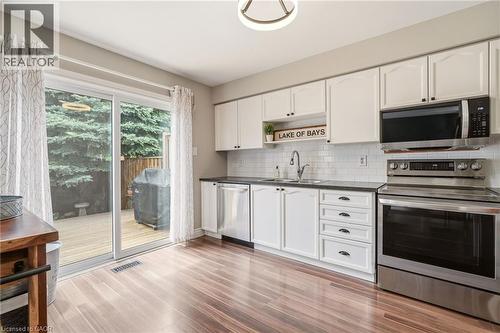 Kitchen featuring white cabinetry, dark countertops, white subway tile backsplash, and stainless steel appliances - 2089 Broadleaf Crescent, Burlington, ON 