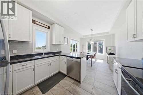 Open-concept kitchen featuring white cabinetry, dark countertops, a subway tile backsplash, stainless steel appliances, and large format floor tiles - 104 Sonoma Valley Crescent, Hamilton, ON - Indoor Photo Showing Kitchen