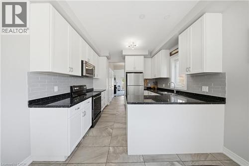 Kitchen featuring white cabinetry with silver-tone hardware, black speckled countertops, gray subway tile backsplash, and stainless steel appliances - 104 Sonoma Valley Crescent, Hamilton, ON - Indoor Photo Showing Kitchen With Upgraded Kitchen