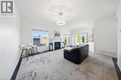 Spacious living area featuring dark wood-finish flooring, a contemporary fireplace with a white mantel, and multiple windows providing natural light - 104 Sonoma Valley Crescent, Hamilton, ON - Indoor With Fireplace