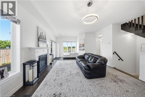 Bright living area featuring dark wood-finish flooring, a white mantel fireplace, and large windows - 104 Sonoma Valley Crescent, Hamilton, ON - Indoor Photo Showing Living Room With Fireplace