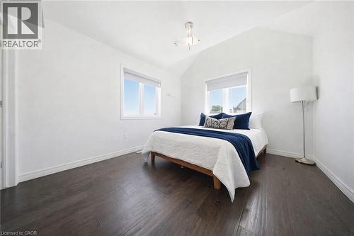 Bedroom featuring a vaulted ceiling with a semi-flush mount fixture, two windows with roller shades, dark wood-finish flooring, and white baseboards - 104 Sonoma Valley Crescent, Hamilton, ON - Indoor Photo Showing Bedroom