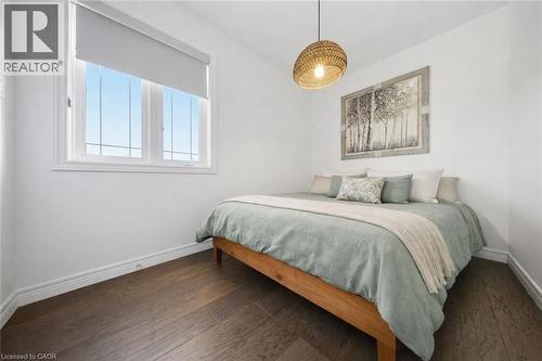 Bedroom featuring wood-finish flooring, white baseboards, a single window with a roller shade, and a woven pendant light fixture - 104 Sonoma Valley Crescent, Hamilton, ON - Indoor Photo Showing Bedroom