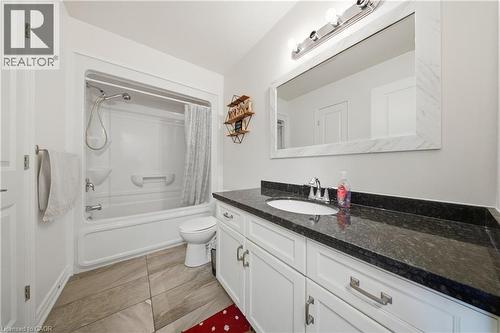 Bathroom featuring a dark granite-style countertop, white cabinetry with silver-tone hardware, and a large framed mirror with integrated vanity lighting - 104 Sonoma Valley Crescent, Hamilton, ON - Indoor Photo Showing Bathroom