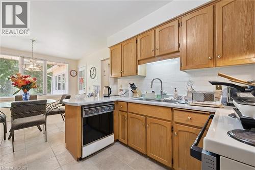 Functional kitchen featuring wood cabinetry, white tile backsplash, a stainless steel sink, and a built-in dishwasher - 176 Sandford Fleming Drive, Waterloo, ON - Indoor Photo Showing Kitchen With Double Sink