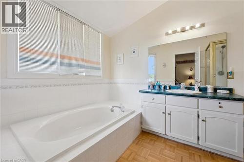 Bathroom featuring a built-in soaking tub with white tile surround, a spacious vanity with a teal countertop and integrated sink, white cabinetry with storage, and wood-finish parquet flooring - 176 Sandford Fleming Drive, Waterloo, ON - Indoor Photo Showing Bathroom