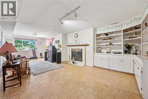 Spacious interior room featuring parquet wood flooring, a central fireplace with a mantel, built-in shelving, white cabinetry, and a large window with vertical blinds - 176 Sandford Fleming Drive, Waterloo, ON - Indoor With Fireplace