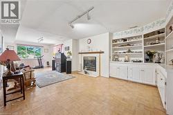 Spacious interior room featuring parquet wood flooring, a central fireplace with a mantel, built-in shelving, white cabinetry, and a large window with vertical blinds - 