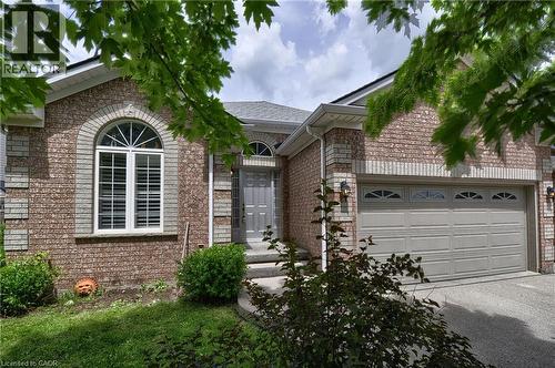 Brick exterior featuring a two-car garage with arched window inserts, an arched entry window with louvered shutters, a gray front door, and mature landscaping - 95 Drinkwater Drive, Cambridge, ON - Outdoor