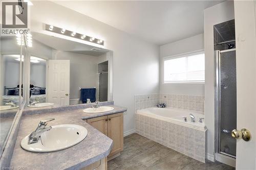 Bathroom featuring a spacious dual-sink vanity with light-colored countertops, a large soaking tub with tiled surround, a separate glass-enclosed shower, wood-finish flooring, and a multi-bulb vanity - 95 Drinkwater Drive, Cambridge, ON - Indoor Photo Showing Bathroom