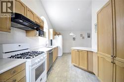 Kitchen featuring light wood cabinetry, white countertops, tile backsplash, and stainless steel dishwasher - 