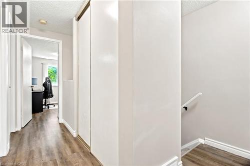 Hallway featuring wood-finish flooring, white baseboards, a white handrail, and white bi-fold closet doors - 175 Siebert Avenue Unit# 9, Kitchener, ON 