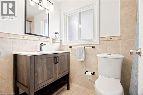 Bathroom featuring a wood-finish vanity with a white countertop and integrated sink, brushed nickel faucet, tiled walls with decorative accents, and a rectangular mirror with a modern light fixture - 175 Siebert Avenue Unit# 9, Kitchener, ON 