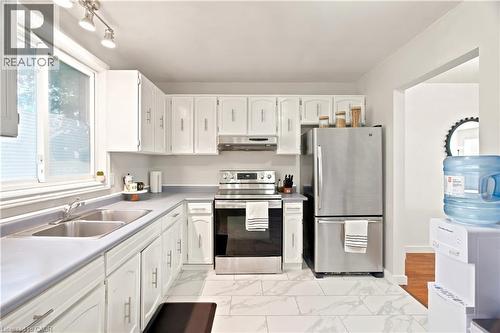 Kitchen featuring white cabinetry with silver hardware, light gray countertops, stainless steel appliances, and white marble-look tile flooring - 175 Siebert Avenue Unit# 9, Kitchener, ON 