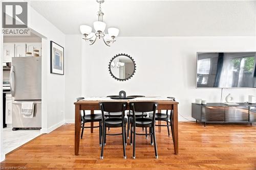Dining area featuring wood-finish flooring, a contemporary chandelier, and an entryway to the kitchen with a stainless steel refrigerator and white cabinetry - 175 Siebert Avenue Unit# 9, Kitchener, ON 