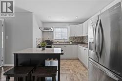 Modern kitchen featuring white cabinetry, stainless steel appliances, a mosaic tile backsplash, and a breakfast bar with stone-finish countertop - 