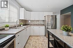 Kitchen featuring white cabinetry, stone-finish countertops, stainless steel appliances, a tiled backsplash, and ceramic tile flooring - 