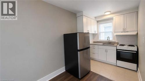 Compact kitchen featuring white shaker cabinetry, stainless steel appliances, a light-toned countertop, and a white subway tile backsplash - 181 King Street E Unit# 9, Kitchener, ON 