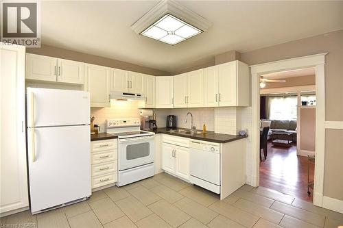 Kitchen featuring white cabinetry, dark countertops, a tile backsplash, and light tile flooring - 56 Barons Avenue N, Hamilton, ON 