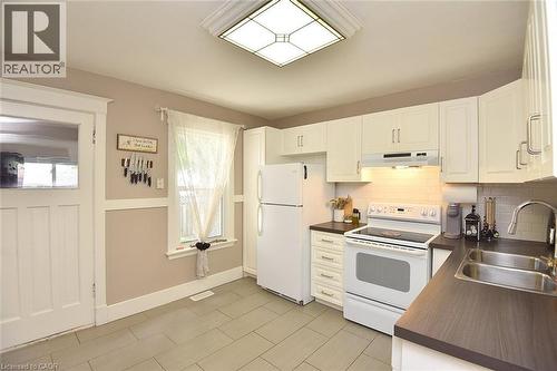 Kitchen featuring white cabinetry, dark countertops, a tile backsplash, and light tile flooring - 56 Barons Avenue N, Hamilton, ON 