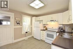Kitchen featuring white cabinetry, dark countertops, a tile backsplash, and light tile flooring - 