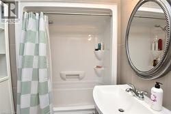 Bathroom featuring a white integrated tub and shower unit, a wall-mounted sink with a chrome faucet, a decorative oval mirror, and vertical wall tiling - 