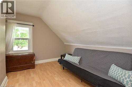 Attic space featuring light wood-finish flooring, a white-trimmed window, and a sloped ceiling - 56 Barons Avenue N, Hamilton, ON 