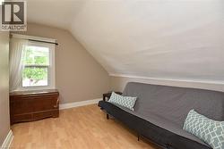 Attic space featuring light wood-finish flooring, a white-trimmed window, and a sloped ceiling - 