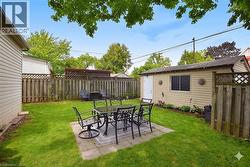Expansive backyard featuring a lush lawn, a paved patio area, and a detached beige-sided shed with a side entry door and a window - 